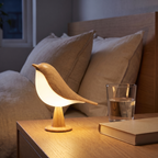 Lampe Oiseau bois clair sur une table de chevet, aussi haute que le verre d'eau à côté