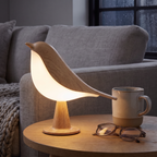 Lampe Oiseau bois clair sur une table d'appoint près du canapé, avec un mug et des lunettes